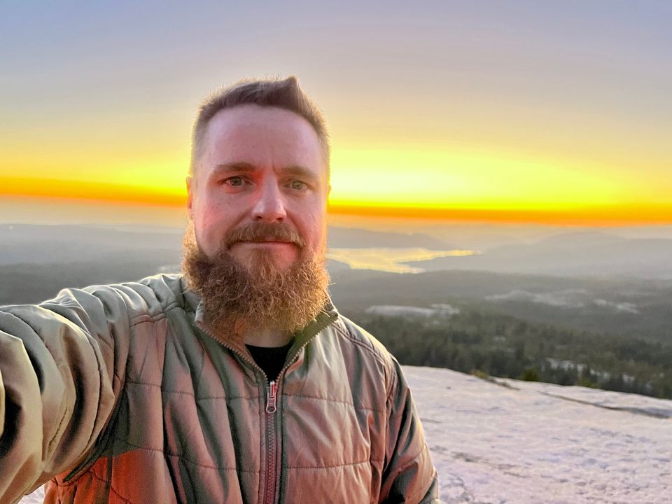 Jeff Wesson standing atop a granite mountain overlooking a lake surrounded by evergreens at sunset.